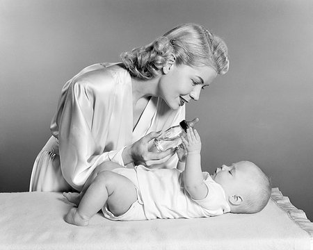 simsearch:846-09181587,k - 1950s SMILING BLOND WOMAN MOTHER WEARING DRESSING GOWN GIVING BABY BOTTLE FEEDING TO INFANT GIRL DAUGHTER Stock Photo - Rights-Managed, Code: 846-09181579