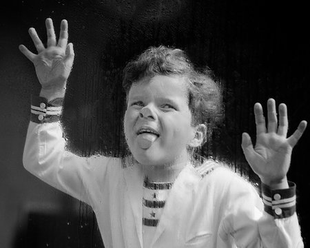 1930s ODD LAUGHING CURLY HAIR BOY WEARING NAUTICAL STYLE SHIRT PLACING HANDS AND STICKING TONGUE ON RAIN WET WINDOW GLASS PANE Stock Photo - Rights-Managed, Code: 846-09181683