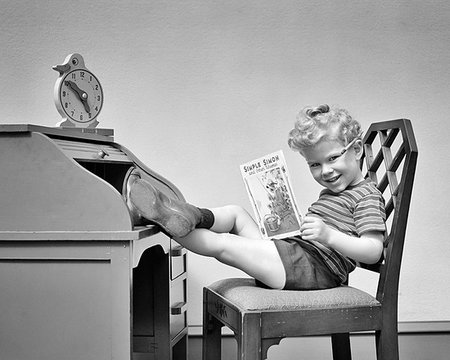 simsearch:846-09181636,k - 1940s CURLY HAIR BLOND BOY PLAYING BOSS SITTING FEET UP ON ROLLTOP DESK CLOCK ON TOP READING BOOK LOOKING AT CAMERA SMILING Stock Photo - Rights-Managed, Code: 846-09181712