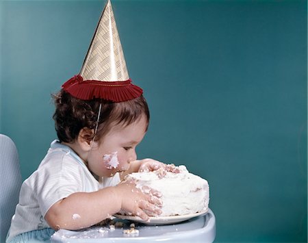 1960s BABY IN HIGHCHAIR WEARING BIRTHDAY HAT EATING WHOLE BIRTHDAY CAKE Foto de stock - Con derechos protegidos, Código: 846-02794021