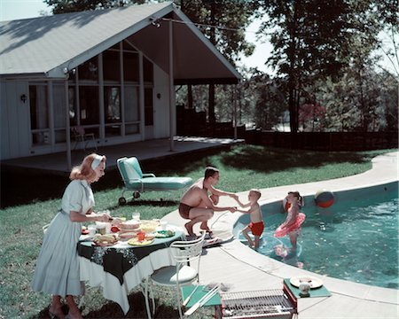 1950s FAMILY OF 4 BACKYARD SWIMMING POOL HOUSE MOM SERVING FOOD MEAL AT TABLE BY GRILL DAD BOY GIRL SUMMER LAWN FURNITURE Foto de stock - Con derechos protegidos, Código: 846-02794087