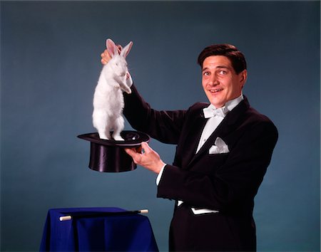 rabbit in man hand - MAGICIAN MAN BLACK COAT BLUE BACKGROUND PULLING RABBIT OUT OF TOP HAT TRICK MAGIC ILLUSION SLEIGHT OF HAND Stock Photo - Rights-Managed, Code: 846-02794102