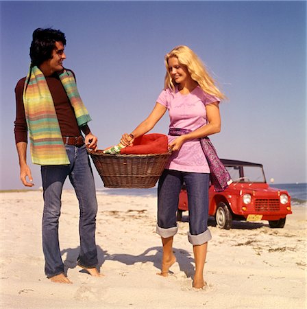 PLAGE DE COUPLE DES ANNÉES 1970 PORTER PANIER PIQUE-NIQUE ROUGE DUNE BUGGY EN ARRIÈRE-PLAN Photographie de stock - Rights-Managed, Code: 846-02794131