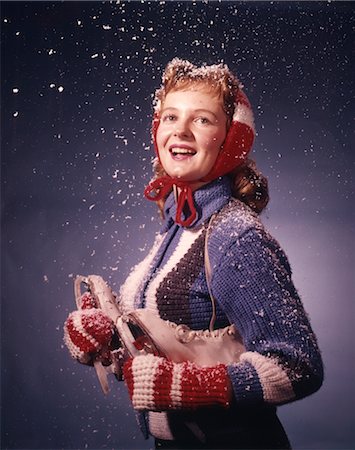 ANNÉES 1960 SOURIANTE JEUNE FEMME PORTANT DES MITAINES ROUGES OREILLE MANCHONS BLEU PULL TENANT DES PATINS À GLACE DANS LA NEIGE QUI TOMBE Photographie de stock - Rights-Managed, Code: 846-02794258