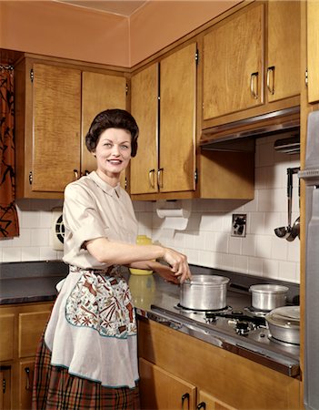 simsearch:846-03164687,k - 1960s SMILING WOMAN HOUSEWIFE WEARING AN APRON STIRRING COOKING POT AT KITCHEN STOVE Foto de stock - Direito Controlado, Número: 846-02794356