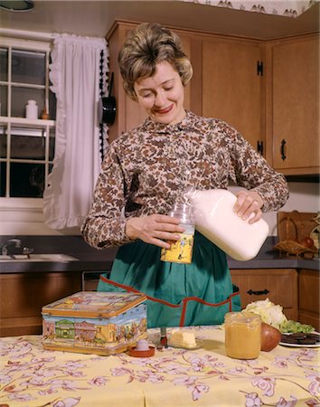 family lunch in home - 1960s SMILING WOMAN HOUSEWIFE MOTHER WEARING APRON IN KITCHEN POURING MILK INTO THERMOS FOR SCHOOL LUNCH Stock Photo - Rights-Managed, Code: 846-02794360