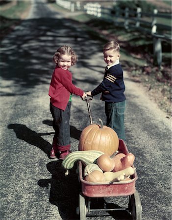 1950s TWO SMILING YOUNG KIDS BOY GIRL IN BLUE JEANS PULLING RED WAGON FULL OF HARVEST PUMPKINS AND GOURDS Stock Photo - Rights-Managed, Code: 846-02794371