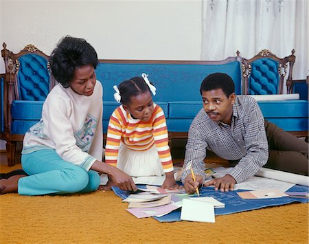 FAMILLE AFRO-AMÉRICAIN DES ANNÉES 1960, ASSIS SUR LE PLANCHER DU SALON À LA RECHERCHE DE NOUVEAUX PLANS DE MAISON Photographie de stock - Rights-Managed, Code: 846-02794482