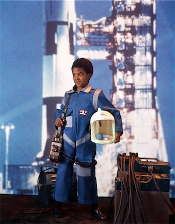 1970s AFRICAN AMERICAN BOY WEARING ASTRONAUT SPACE SUIT COSTUME HELMET ROCKET MISSILE BACKGROUND CAREER Stock Photo - Rights-Managed, Code: 846-02794530