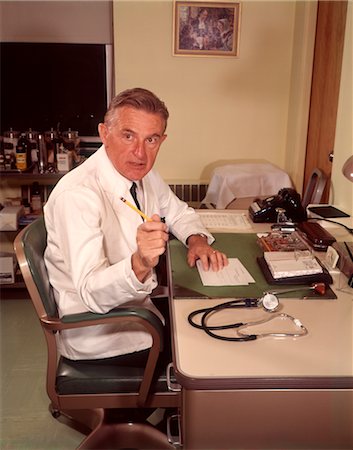 doctor vintage - 1960s MAN DOCTOR POINTING GESTURING WITH PENCIL SEATED AT DESK IN OFFICE Stock Photo - Rights-Managed, Code: 846-02794702