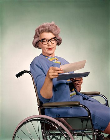 1960s SENIOR WOMAN WEARING GLASSES SITTING IN WHEELCHAIR READING INSURANCE CHECK Stock Photo - Rights-Managed, Code: 846-02794721