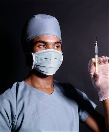 simsearch:846-02794819,k - 1970s AFRICAN AMERICAN MAN DOCTOR NURSE SURGICAL MASK GOWN GLOVES HOLDING HYPODERMIC SYRINGE NEEDLE PREPARING INJECTION SHOT Stock Photo - Rights-Managed, Code: 846-02794800