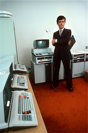 1980s RETRO MAN COMPUTER PROGRAMMER STANDING IN A ROOM WITH EARLY TEXAS INSTRUMENTS HARDWARE SCREENS KEYBOARDS Stock Photo - Rights-Managed, Code: 846-02794908