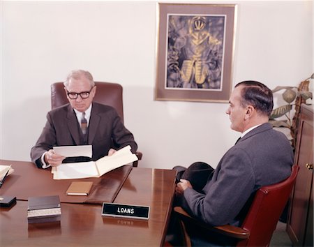 1960s MAN TALKING TO BANKER LOAN OFFICER LOANS BANK DESK Foto de stock - Con derechos protegidos, Código: 846-02794914