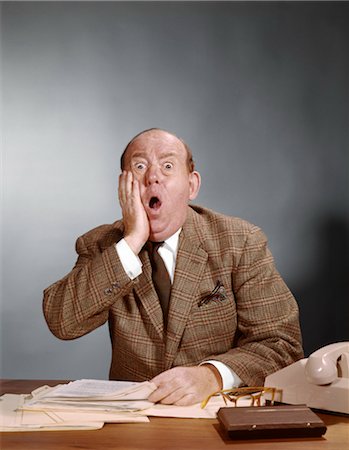 simsearch:846-02796149,k - 1960s SHOCKED BALDING EXECUTIVE WITH HAND TO CHEEK SITTING AT DESK Stock Photo - Rights-Managed, Code: 846-02794983