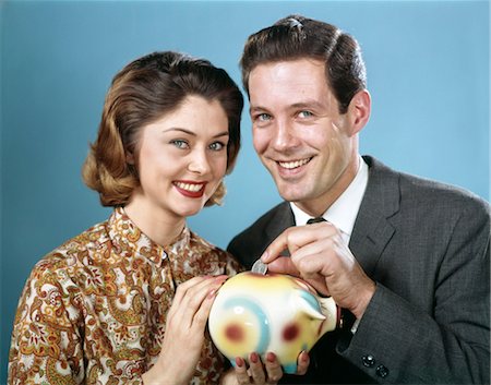 1950s 1960s SMILING YOUNG COUPLE MAN AND WOMAN PUT QUARTER IN SAVINGS PIGGY BANK Foto de stock - Con derechos protegidos, Código: 846-02795009