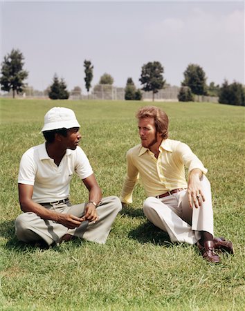 1970s TWO MEN CASUAL CLOTHES SITTING IN GRASSY FIELD TALKING ONE MAN AFRICAN AMERICAN OTHER CAUCASIAN Stock Photo - Rights-Managed, Code: 846-02795066