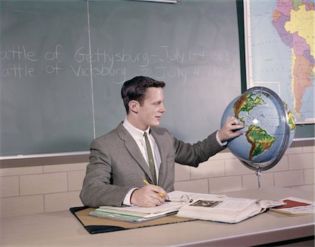 1960s MAN STUDENT TEACHER POINT AT GLOBE AT DESK NOTEBOOK BOOK PAPERS WEAR SUIT & TIE CHALKBOARD STUDY HISTORY GEOGRAPHY Foto de stock - Con derechos protegidos, Código: 846-02795089