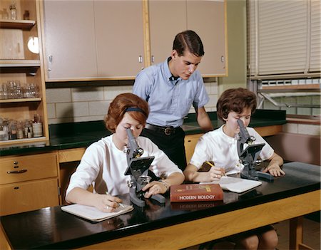 simsearch:846-02796432,k - 1960s 3 STUDENTS BIOLOGY CLASSROOM LAB GIRLS LOOK INTO MICROSCOPES BOY STAND LOOK OVER SHOULDER TEXTBOOK Stock Photo - Rights-Managed, Code: 846-02795135