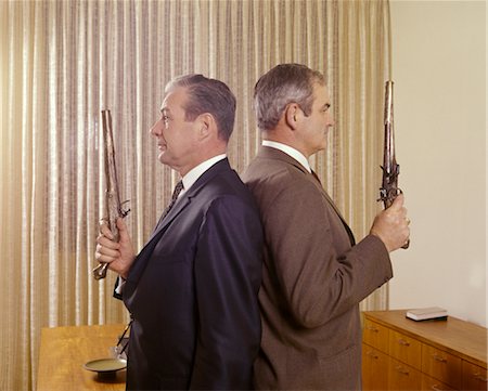 fight fires - 1960s 2 MIDDLE AGED BUSINESS MEN STAND BACK TO BACK HOLDING GUNS DUEL PISTOLS Stock Photo - Rights-Managed, Code: 846-02795167