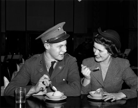 simsearch:846-02792171,k - 1940ER JAHRE LÄCHELND PAAR MANN SOLDAT IN ARMY UNIFORM UND FRAU FREUNDIN SITZEN AN SODA FOUNTAIN COUNTER ESSEN SCHÜSSEL MIT EIS Stockbilder - Lizenzpflichtiges, Bildnummer: 846-02795410