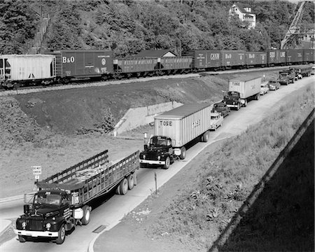 simsearch:846-03164267,k - 1950s LINE OF TRAFFIC WITH MANY TRUCKS & CARS & FREIGHT TRAIN PASSING ON ADJACENT HILLSIDE Stock Photo - Rights-Managed, Code: 846-02795437