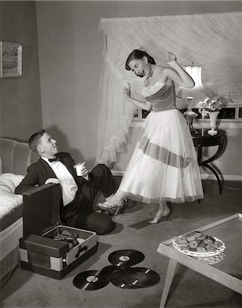 stereo - ANNÉES 1960 ANNÉES 1950 TEEN COUPLE IN LIVING ROOM IN PROM DRESS & SMOKING GUY ASSIS SUR LE PLANCHER & FILLE DANSANT SUR LES NOTES D'UN TOURNE-DISQUE Photographie de stock - Rights-Managed, Code: 846-02795439