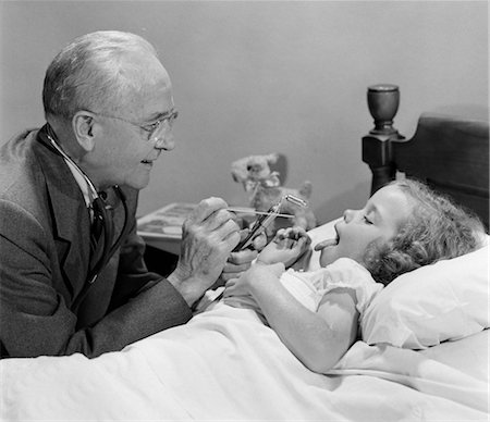 1950s LITTLE GIRL SICK IN BED STICKING OUT HER TONGUE DOCTOR ON AT HOUSE CALL AT BED SIDE LOOKING AT HER THROAT Foto de stock - Con derechos protegidos, Código: 846-02795514