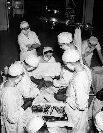 simsearch:846-02794801,k - 1930s SURGERY TEAM WEARING WHITE GOWNS CAPS AND MASKS IN HOSPITAL OPERATING ROOM PERFORMING A MEDICAL PROCEDURE Foto de stock - Con derechos protegidos, Código: 846-02795569