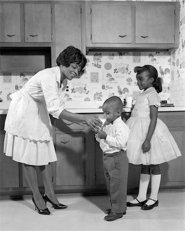 1960s SMILING AFRICAN AMERICAN WOMAN MOTHER IN APRON AND PUMPS GIVING A GLASS OF MILK TO SON AND DAUGHTER WITH MARY JANE SHOES Foto de stock - Con derechos protegidos, Código: 846-02795692