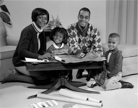 ANNÉES 1960 FAMILLE AFRO-AMÉRICAINE SOURIANT ASSIS DERRIÈRE UNE TABLE À CAFÉ EN REGARDANT BLUEPRINTS Photographie de stock - Rights-Managed, Code: 846-02795702