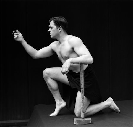 simsearch:846-02797122,k - 1920s MALE MAN SEMI NUDE CLASSICAL POSE ON ONE KNEE HAND FORWARD OTHER RESTS ON LONG ARMED HAMMER RETRO VINTAGE Stock Photo - Rights-Managed, Code: 846-02795739