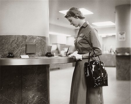 simsearch:846-02796076,k - 1950s 1960s WOMAN HANDBAG ON ARM GLOVES FILLING OUT DEPOSIT SLIP BANK COUNTER Stock Photo - Rights-Managed, Code: 846-02795764