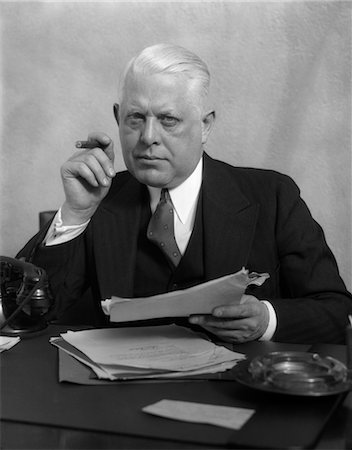 simsearch:846-02795784,k - 1930s MAN IN OFFICE SITTING AT DESK HOLDING PAPERS SMOKING A CIGAR Stock Photo - Rights-Managed, Code: 846-02795762