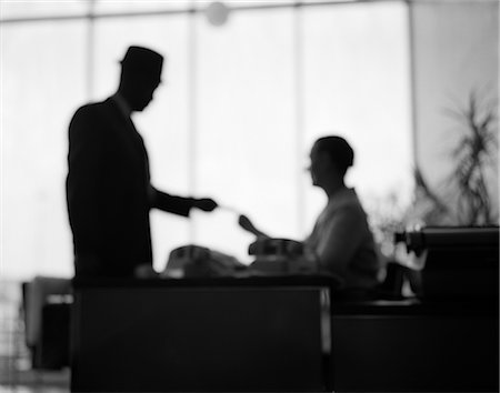 simsearch:846-02796823,k - 1960s BLURRED BLURRY UN-SHARP SILHOUETTED FIGURES MAN SALESMAN IN HAT HANDING HIS BUSINESS CARD TO WOMAN RECEPTIONIST Stock Photo - Rights-Managed, Code: 846-02795855