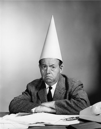 stress black & white portrait - 1960s UNHAPPY BUSINESSMAN BEHIND DESK WEARING DUNCE CAP LOOKING AT CAMERA Stock Photo - Rights-Managed, Code: 846-02795862