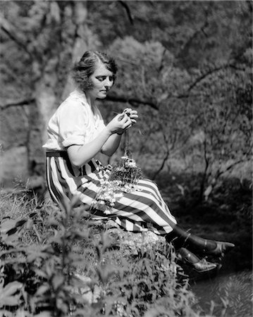 1920s YOUNG WOMAN IN STRIPED SKIRT SITTING ON STREAM BANK IN WOODS BRAIDING GARLAND OF WILD FLOWERS Stock Photo - Rights-Managed, Code: 846-02795936