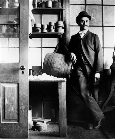 TOUR DES ANNÉES 1890 DU XXE SIÈCLE DE LA SIÈCLE HOMME EN COSTUME & BOWLER PENCHÉE SUR LE TONNEAU EN BOIS SUR TABLE Photographie de stock - Rights-Managed, Code: 846-02795984