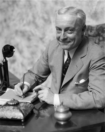 1920s 1930s SMILING MAN BUSINESSMAN SALESMAN SITTING AT DESK SMOKING CIGAR WRITING A MEMO Stock Photo - Rights-Managed, Code: 846-02796017