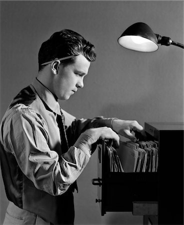 fichero - 1940s YOUNG MAN OFFICE FILE CLERK PUTTING RECORDS INTO FILING CABINET DRAWER Foto de stock - Con derechos protegidos, Código: 846-02796013