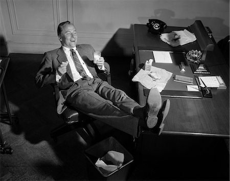 1950s SMILING MAN BUSINESSMAN SALESMAN EATING LUNCH IN OFFICE WITH FEET RESTING UP ON DESK Foto de stock - Con derechos protegidos, Código: 846-02796086