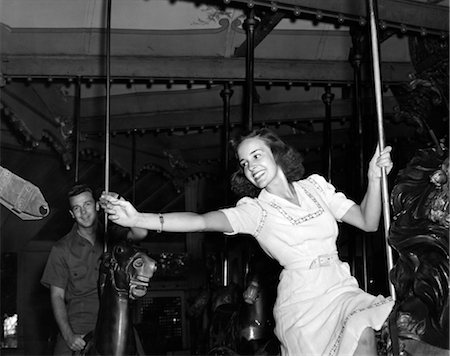 fiera - 1940s WOMAN ON CAROUSEL REACHING FOR BRASS RING MAN IN BACKGROUND INDOOR Fotografie stock - Rights-Managed, Codice: 846-02796154