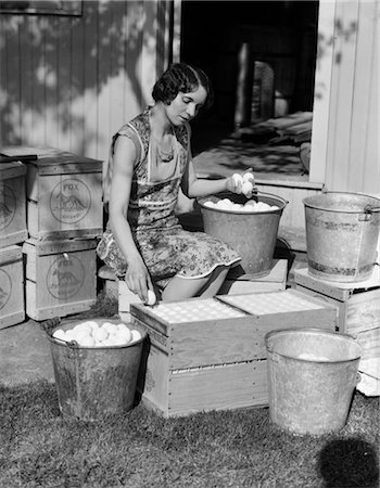 1930s WOMAN FARM WIFE SITTING OUTSIDE OF HEN HOUSE DOORWAY PUTTING EGGS FROM PAILS INTO SHIPPING CRATES Foto de stock - Con derechos protegidos, Código: 846-02796158