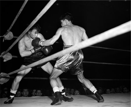 1950s BOXING MATCH SHOWN BETWEEN ROPES FROM FLOOR WITH ONE FIGHTER THROWING PUNCH & OTHER DUCKING Stock Photo - Rights-Managed, Code: 846-02796175
