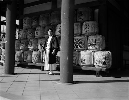 sake - 1920s 1930s JAPANESE MAN IN ROBES PRIEST STANDING AMID SACRED SAKE RICE WINE CASKS AT HEIAN SHRINE JAPAN Stock Photo - Rights-Managed, Code: 846-02796336