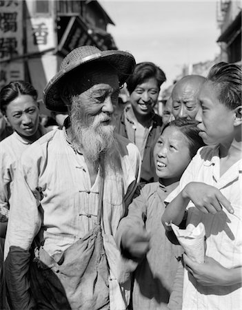 1920s 1930s ELDERLY OLD CHINESE MAN WITH BEARD WEARING STRAW COOLIE HAT TALKING WITH YOUNG PEOPLE Foto de stock - Con derechos protegidos, Código: 846-02796400