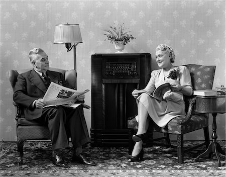 radio - ANNÉES 1940 SENIOR COUPLE ASSIS DANS LE SALON LECTURE JOURNAUX ET DE MAGAZINES À L'ÉCOUTE DE LA RADIO Photographie de stock - Rights-Managed, Code: 846-02796567