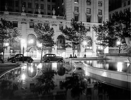 1930s NIGHT SCENE 5TH AVENUE HOTEL FRONT TREE LINED SIDEWALK MOTORCARS POOL AND PEDESTRIANS STREET LAMPS REFLECTING ON SURFACES Stock Photo - Rights-Managed, Code: 846-02796587