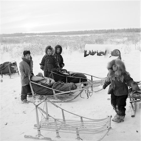 1960s GROUP OF ESKIMO CHILDREN DRESSED IN FUR PARKERS ON THE FROZEN TUNDRA WITH THEIR SLEDS Foto de stock - Con derechos protegidos, Código: 846-02796596