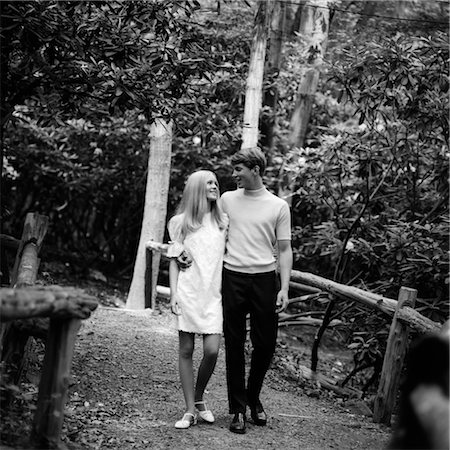 people walking in black and white - 1960s YOUNG COUPLE MAN WOMAN BLOND WALKING OUTSIDE PATH BRIDGE ROMANCE DATE FLIRT NATURE FOREST PARK WOODS Stock Photo - Rights-Managed, Code: 846-02796643